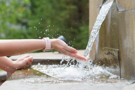 A closeup of elegant womans hands with watch, catching water stream from the stone fountainの写真素材
