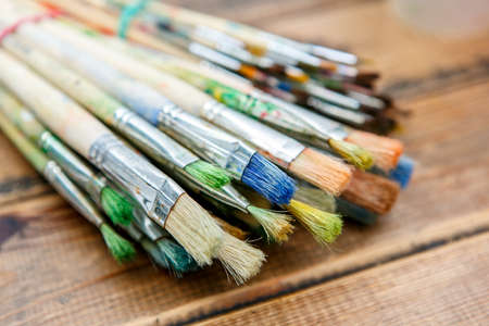 A closeup of the few paintbrushes with traces of paint on them on the wooden tableの写真素材