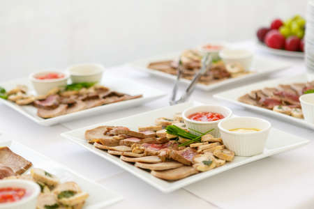 A close up of square plates with meat assorted and sauces on the white table