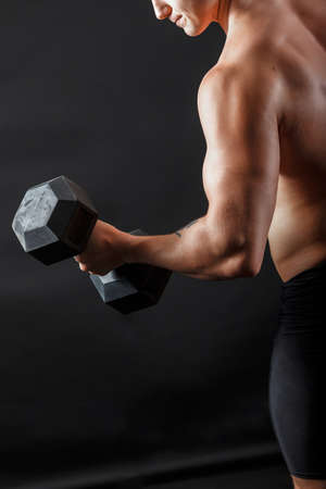 Male bodybuilder in black fitness shorts doing exercise with gymnastic bumbell turn his leftの写真素材