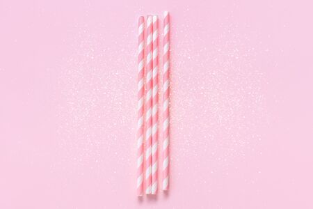 Pastel paper straws with white stripes on soft pink background with sparkles. Festive concept. Flat lay style with copy space.の写真素材
