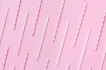 Pattern of pastel paper straws with white stripes and dots on soft pink background. Festive zero waste concept. Flat lay style.の写真素材