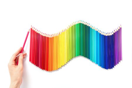Rainbow wave of multicolored pencils isolated on white background. Female hand holds a wood red pencil. Back to school or drawing training concept.の写真素材