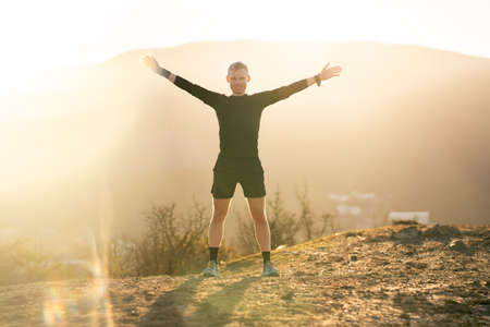 Man standing, smiling with sunrise in mountainsの写真素材