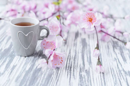 morning breakfast of tea in a cup with a heart with pink flowers in a spring sunny day on a light backgroundの写真素材