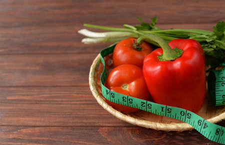 vegetables in a basket on a wooden brown background, tomatoes and red pepper with centimeter diet food for weight loss with vitaminsの写真素材