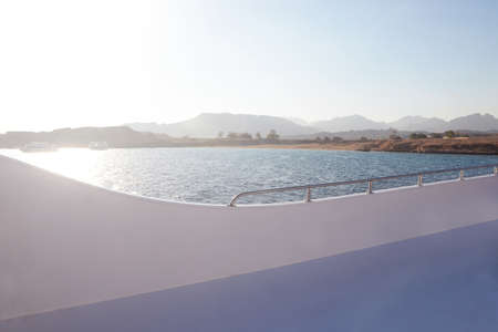 beautiful view of the yacht ship to the sea from the deck on vacation in a cruise with the shore and mountainsの写真素材