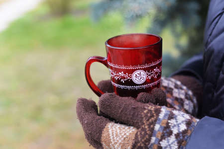 girl holds knitted gloves in mittens askus with a warming drink coffee tea in the winter near the...