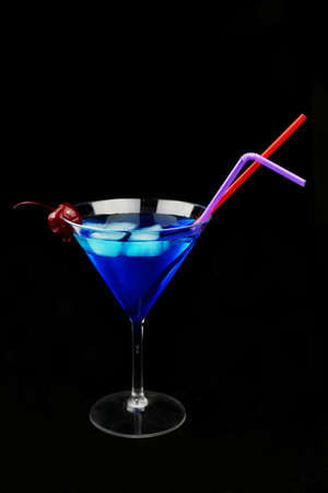 a beautiful glass with a refreshing drink of blue color with ice on an isolated background with a cocktail cherryの写真素材