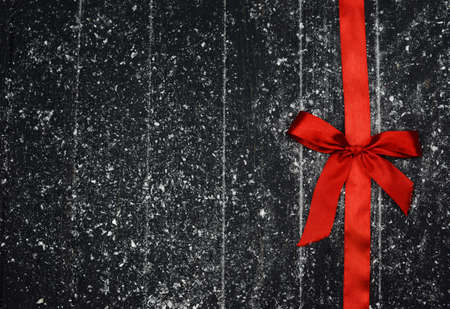 red bow tied with a ribbon textile on a wooden background with snow for the holiday Christmas new...