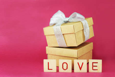 surprise gift box with a bow on a pink background with wooden letters the word love for the holiday Valentine's Dayの写真素材