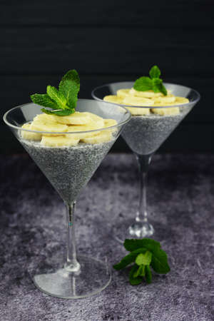 Chia dessert with grains of bananas fruit and leaf of mint in glasses on a dark  backgroundの写真素材