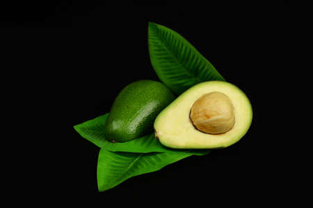 ripe green avocado fruit with half and leaves on a black background