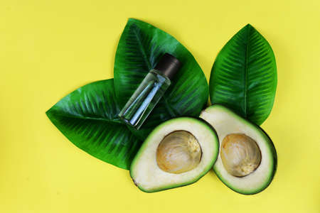 ripe green avocado fruit with cosmetic oil with half and leaves on a yellow background