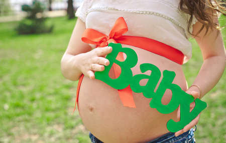 pregnant girl expectant mother with a red bow on her belly holding an  wooden baby letters for...