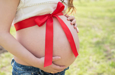 pregnant girl expectant mother holds her belly with a red bow on natureの写真素材