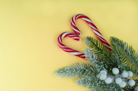 Christmas or New Year festive background with Santa's lollipop cane sticks. White cane with red stripes on a yellow illuminating trend background. with tree branchesの写真素材
