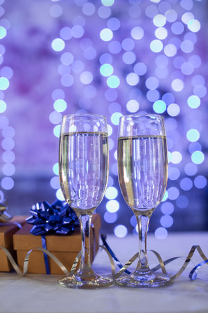 beautiful gift box with a bow with glasses of champagne on a bokeh background for the new year Christmas and birthdayの写真素材