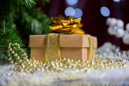 beautiful golden gift box with a bow on the snow for the new year and christmas with decorations and a christmas treeの写真素材