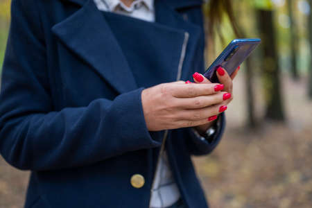 Close-up of a woman in a blue coat holding a smartphone in her hands.の写真素材