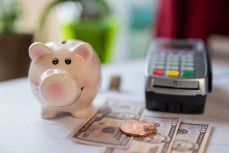 pink piggy bank for money savings coins with dollar bills and a payment terminal for cashless payments or a coin of Internet currency bitcoinの写真素材