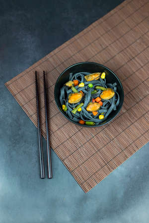 dish noodles black with vegetables and mussels asian food with chopsticksの写真素材