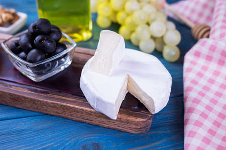 appetizer camembert cheese with olives on a wooden board with honey and grapes on a blue backgroundの写真素材