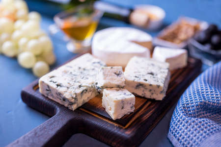 appetizer assorted cheese dor blue and camembert on a wooden board with honey and grapes and olivesの写真素材
