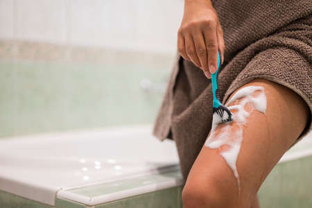 a girl holds a razor in her hands for epilation and hair removal on the body and legs in the bathroomの写真素材