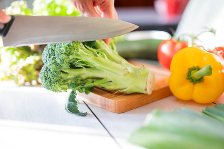 girl cook in the kitchen cuts celery with vegetables on a wooden board with a knifeの写真素材
