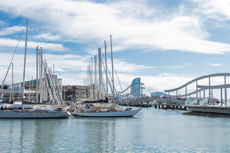 Barcelona Spain, February 19, 2026, Luxury sailboats and yachts moored in Port Vell, Barcelona, Spain. Scenic harbor view with the Rambla del Mar bridge and W Hotel in the background on a sunny day.のeditorial素材