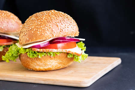 burger with meat cheese tomato onions on a board on a black background.の写真素材