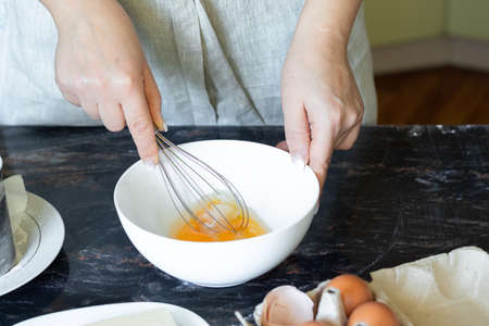 woman beats eggs with a whisk in a white bowl, concept cookingの写真素材