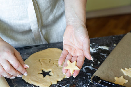 A woman cuts out cookies in the shape of a Christmas tree from the dough, the concept of making Christmas cookies.の写真素材