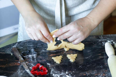 A woman cuts out cookies in the shape of a Christmas tree from the dough, the concept of making...