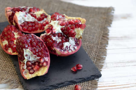 pomegranate fruit open on black slate board, side view, light vintage wooden backgroundの写真素材