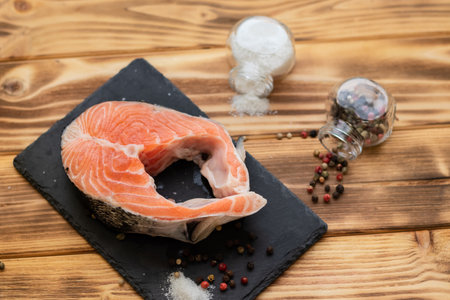 salmon steak on a black slate board on a wooden background view from above next to salt and pepper.の写真素材