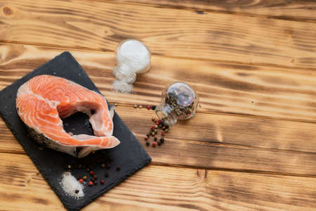 salmon steak on a black slate board on a wooden background view from above next to salt and pepper.copy space.の写真素材