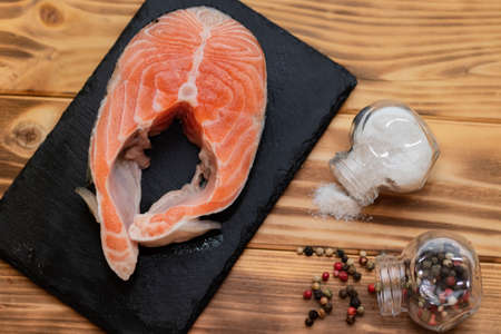 salmon steak on a black slate board on a wooden background view from above next to salt and pepper.の写真素材