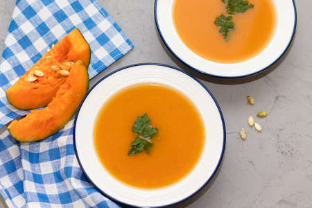 two plates of pumpkin soup on a concrete background and a napkin in a checkered blueの写真素材