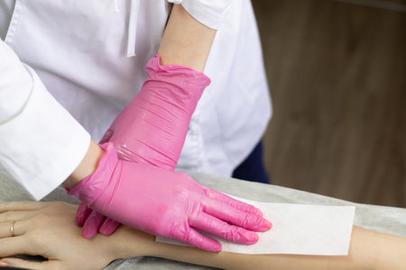 depilation of a womans hands, a master of depilation in pink gloves applies wax to the bodyの写真素材