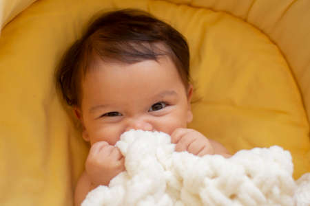 asian baby girl is on her bed playing with white blanketの写真素材