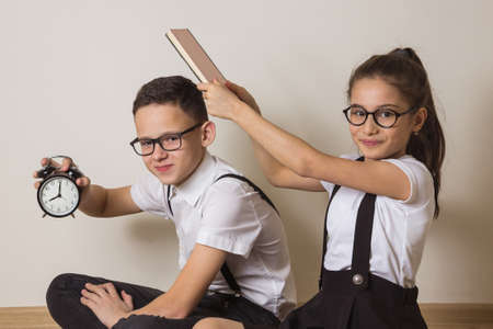 Schoolchildren with book and alarm clock. Funny kids. Boy and girl with glasses.の写真素材