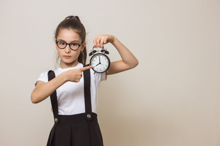 Girl holding an alarm clock. Girl shows her finger at the clock. Space for textの写真素材