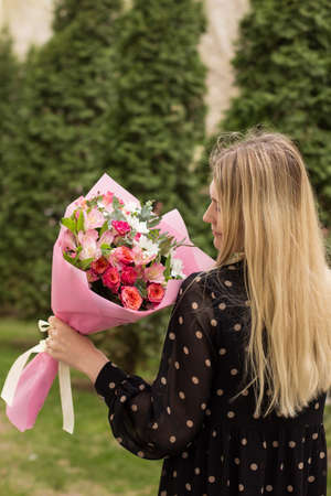 Beautiful girl hold and walk with flower bouquet after delivery in the city. Side view. Real people conceptの写真素材