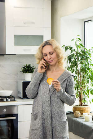 Girl home kitchen talking phone. Girl holding plate and phone hands. Girl holding dried fruit her handsの写真素材