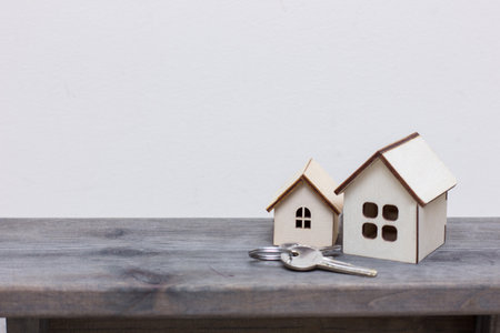 Small wooden houses stand on the board and next to the keys.Wooden houses close-up.Toy houses made of plywood on white background. two houses and keys on the tableの写真素材