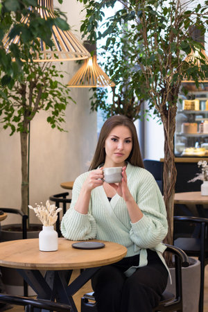girl in a cafe drinks coffee and tea near the window.girl looking out the window in a restaurant.breakfast in a cafeの写真素材