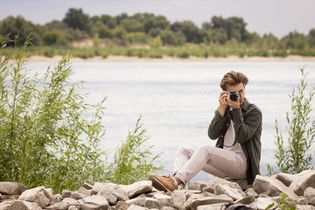 The guy looks into the lens.Young man taking pictures.photography courses.Man holding camera in his hands.Photoshoot.Photographer in nature.Street photography.learning camera settingsの写真素材