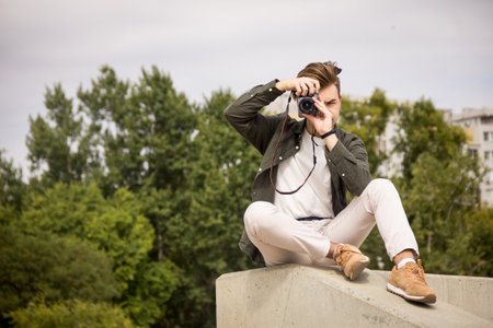 The guy looks into the lens.Young man taking pictures.photography courses.Man holding camera in his hands.Photoshoot.Photographer in nature.Street photography.learning camera settingsの写真素材